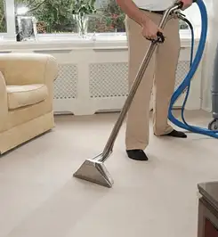 Professional carpet cleaner using a hot-water extraction wand and hose machine in a living room in West Palm Beach, FL.