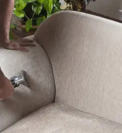 Professional upholstery cleaner deep-cleaning a fabric sofa with a handheld extraction tool and hose West Palm Beach, FL.