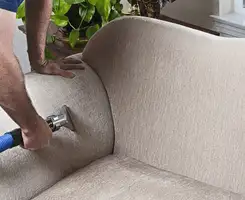 Professional upholstery cleaner deep-cleaning a fabric sofa with a handheld extraction tool and hose in West Palm Beach, FL.